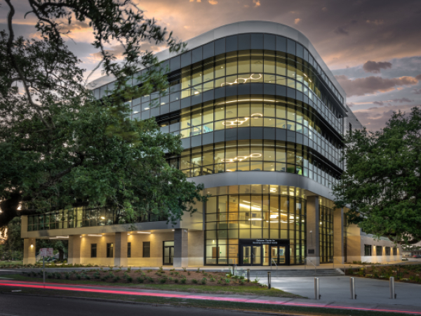 Exterior of a building at dusk with oak trees on either side of the entrance. 
