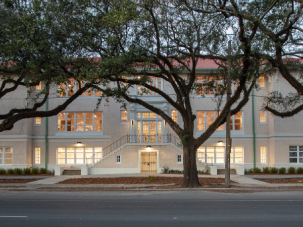 Exterior of a building at dusk with oak trees lining the sidewalk. 