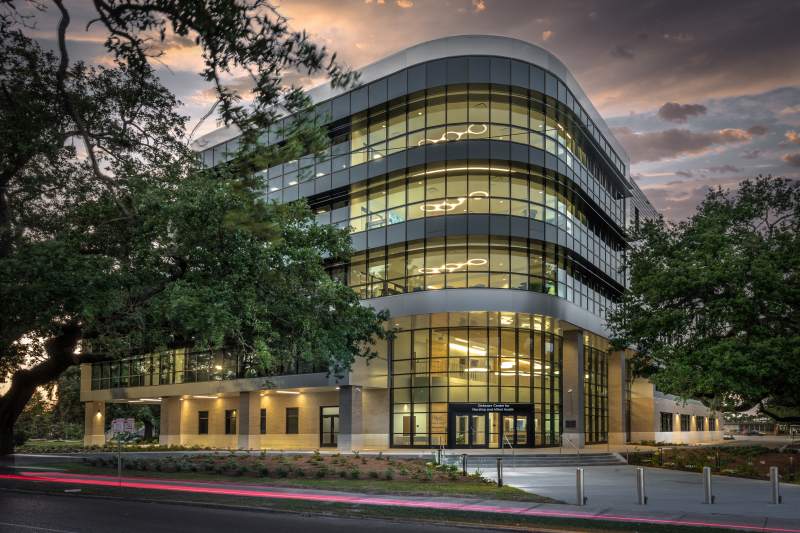 Exterior of a building at dusk with oak trees on either side of the entrance. 