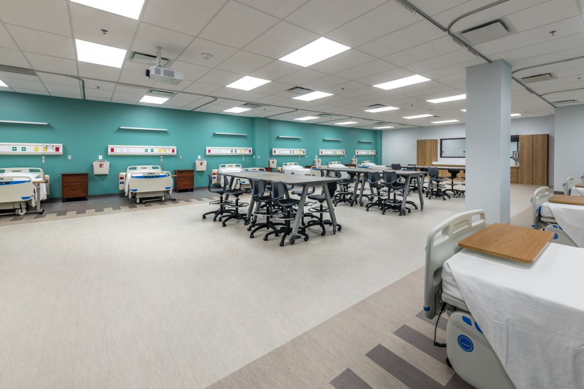 Nursing school classroom with hospital beds and tables. 