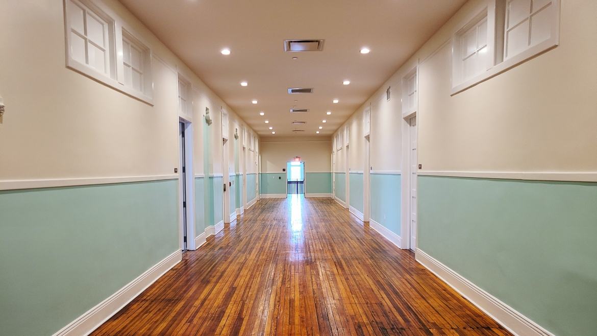 A long hallway with wooden floors and teal and white walls.